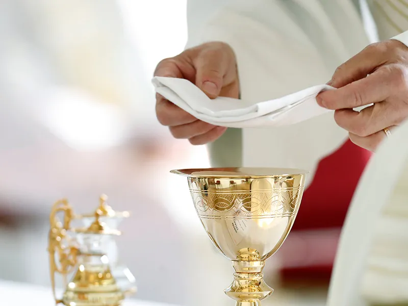 Manos sosteniendo un c&aacute;liz y un pa&ntilde;o blanco en un ritual religioso.