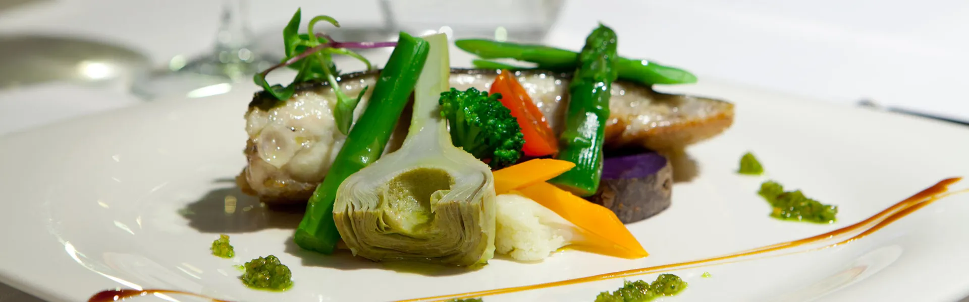 Plato gourmet con verduras y pescado, adornado con salsas.