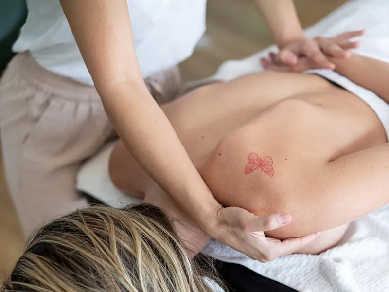 Persona recibiendo masaje en la espalda con tatuaje de mo&ntilde;o rojo visible.