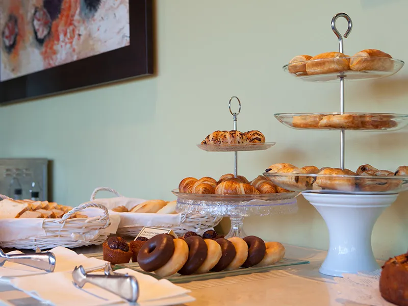Variedad de pasteles y bollos en estantes de una mesa de desayuno.