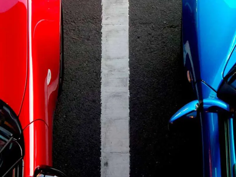 Autos rojo y azul estacionados lado a lado, separados por una l&iacute;nea blanca.