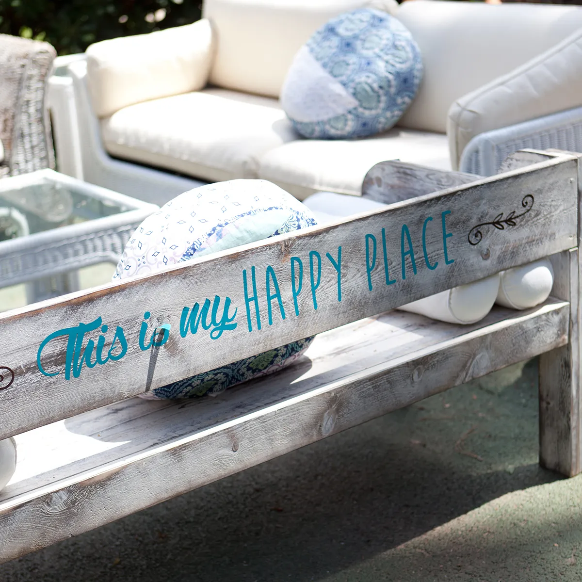 Banco r&uacute;stico con frase: "This is my happy place". De fondo, muebles de exterior.
