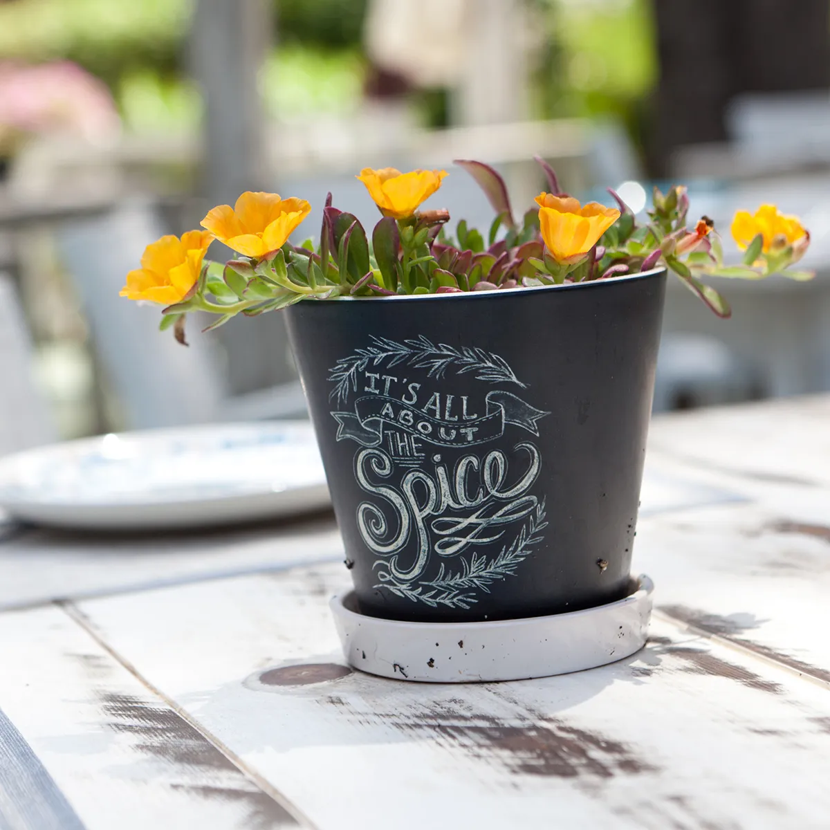 Maceta negra con flores amarillas y texto caligrafiado en la superficie.