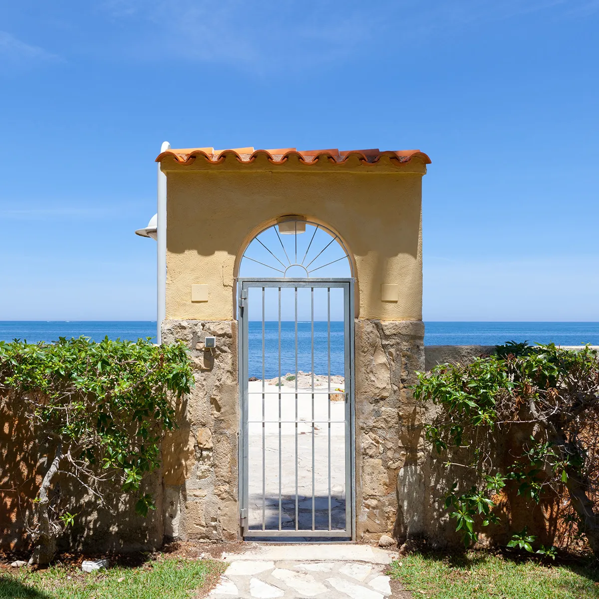 Puerta de hierro y muro, con vista al mar y cielo azul.