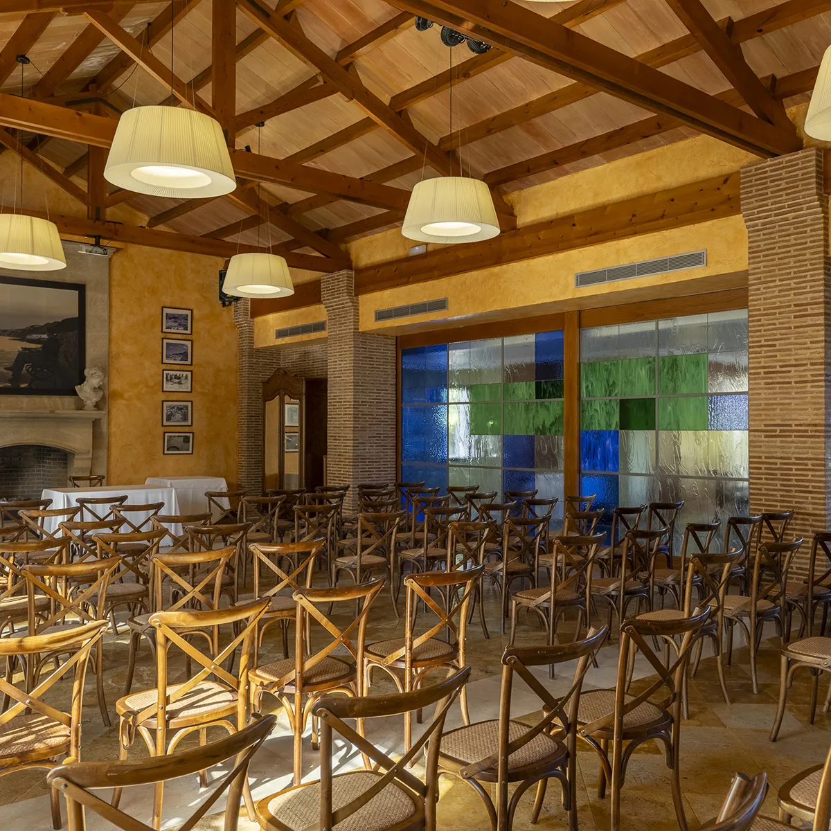 Sala de eventos con sillas de madera y vitrales coloridos en la pared.