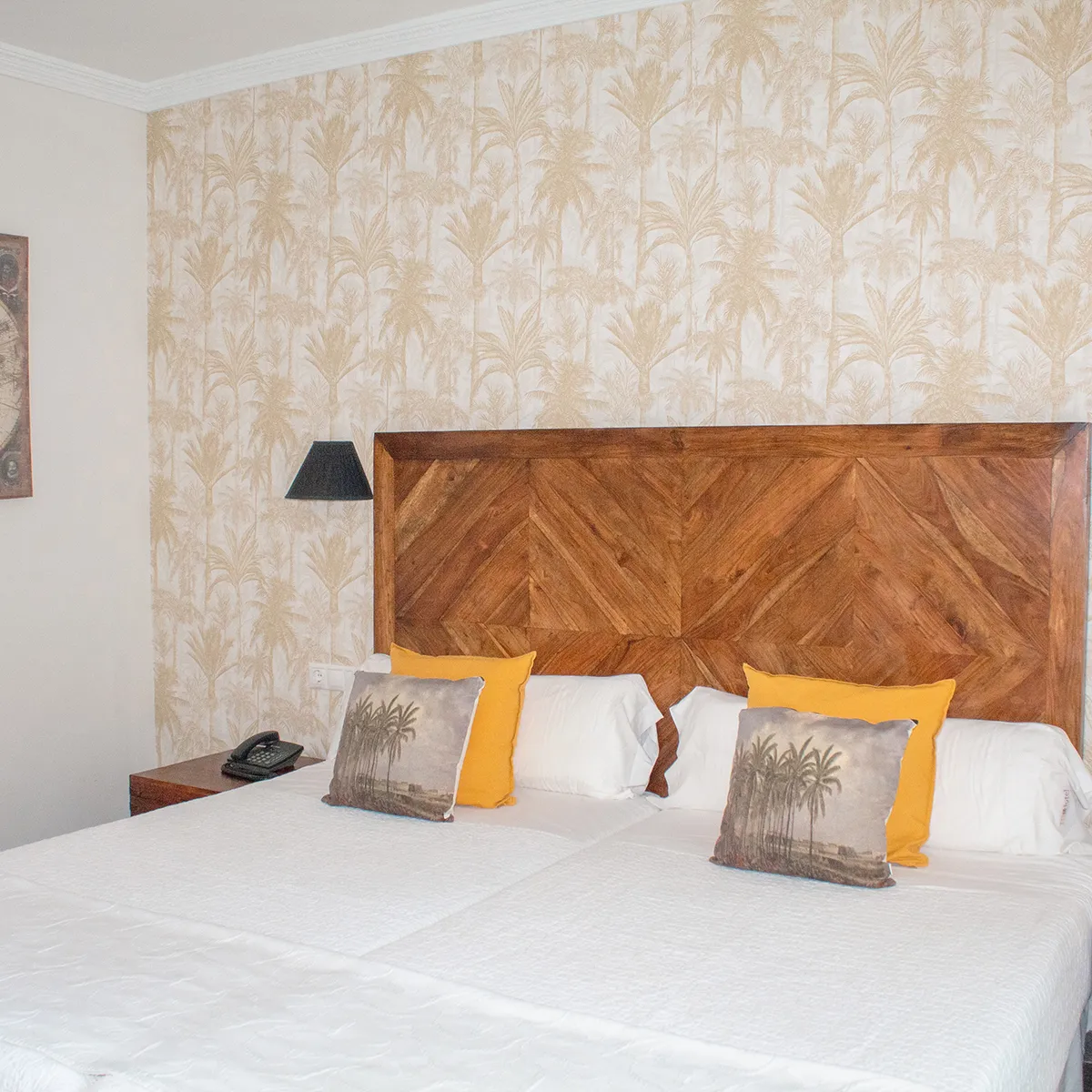 Cama con cabecero de madera, cojines amarillos y pared con papel tapiz de hojas.