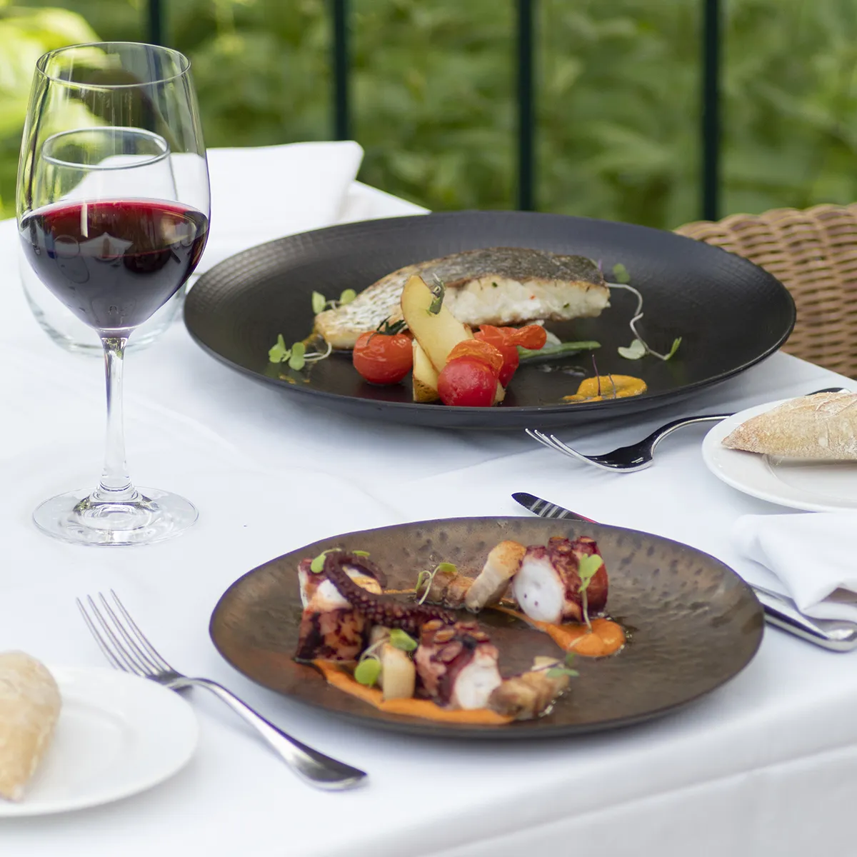 Platos gourmet con vino tinto en mesa elegante al aire libre.