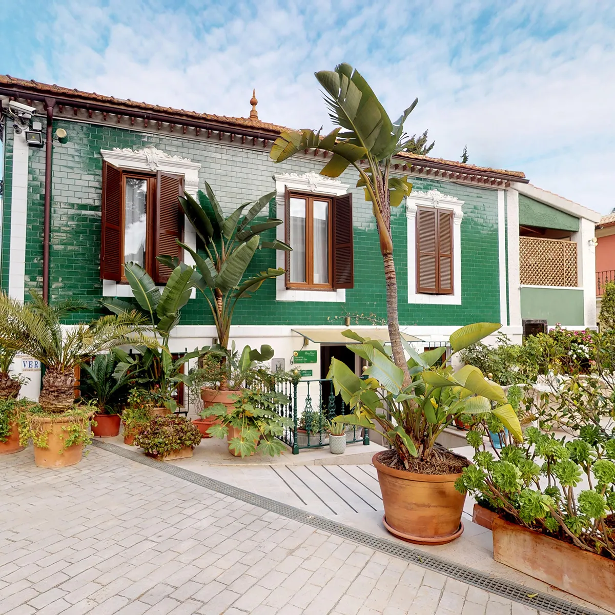 Casa verde con ventanas de madera y plantas en macetas al frente.