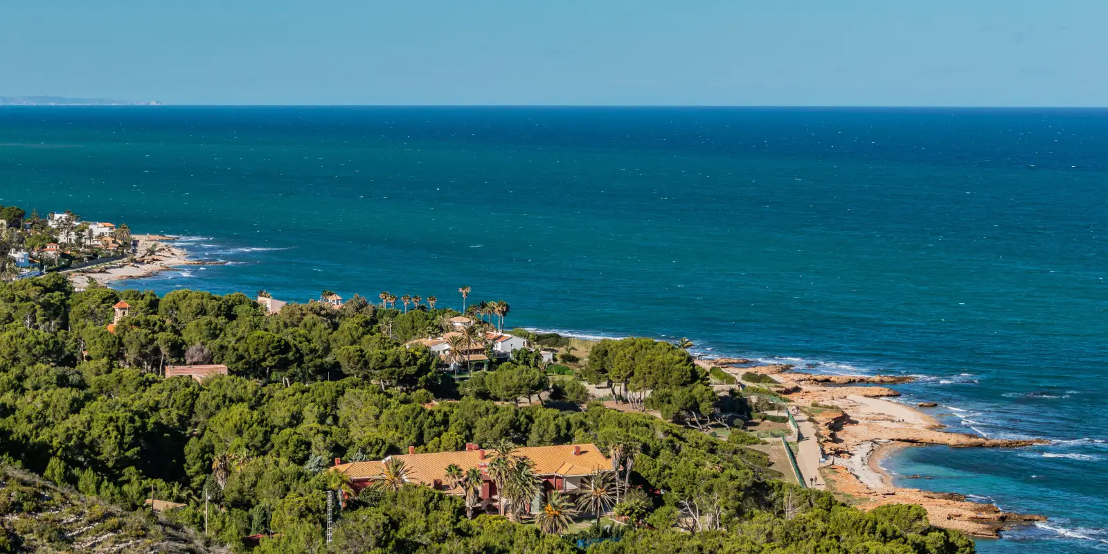 Costa tropical con acantilados verdes, casas y playas junto al mar azul
