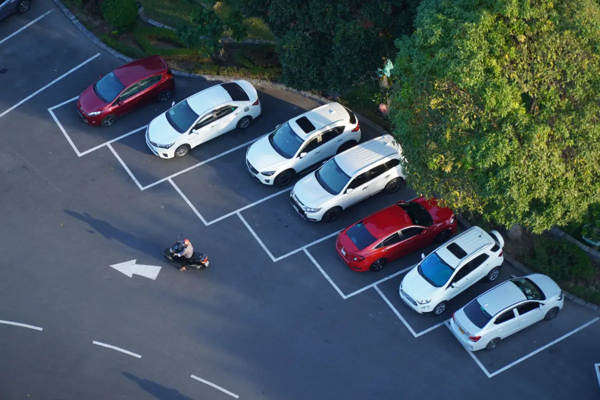 Vista a&eacute;rea de coches estacionados en un parking con &aacute;reas se&ntilde;alizadas y persona
