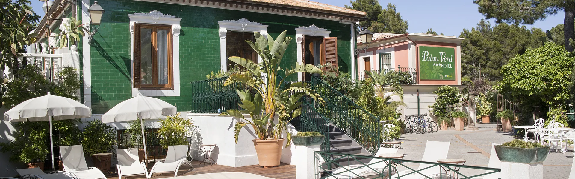 Fachada de un hotel con terraza y vegetaci&oacute;n tropical.