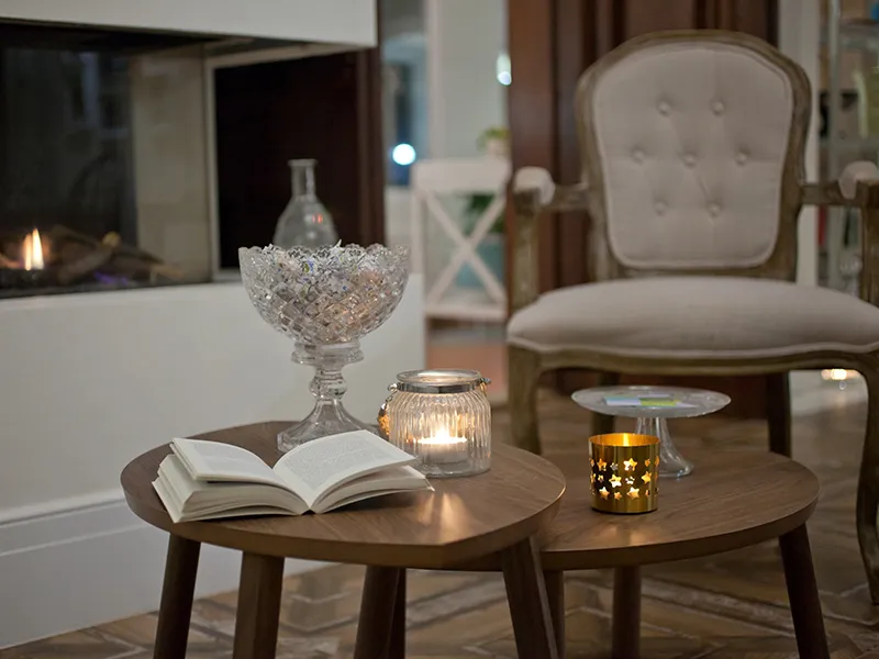 Sala acogedora con libro y velas sobre mesas frente a una chimenea.