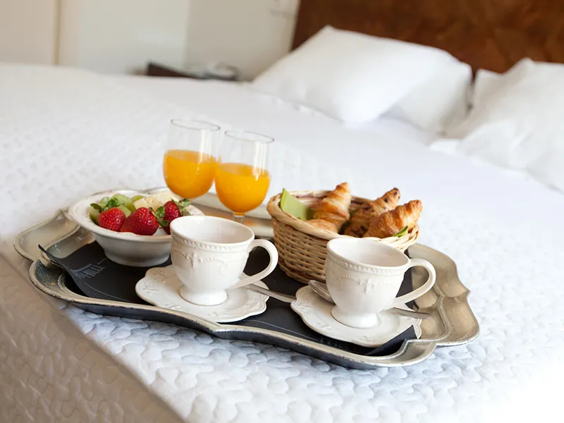 Desayuno en la cama: caf&eacute;, jugo, croissants y fruta en una bandeja.