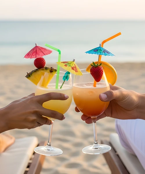 Dos c&oacute;cteles con frutas y sombrillas en la playa al atardecer.