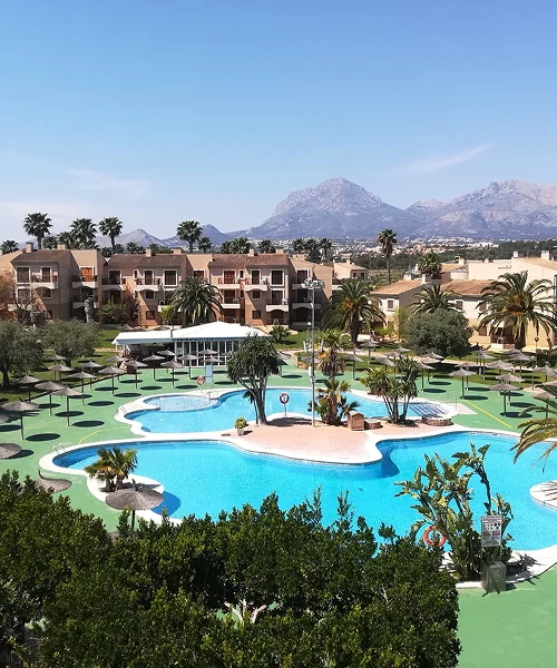 Piscina en complejo vacacional rodeado de palmeras y monta&ntilde;as al fondo.
