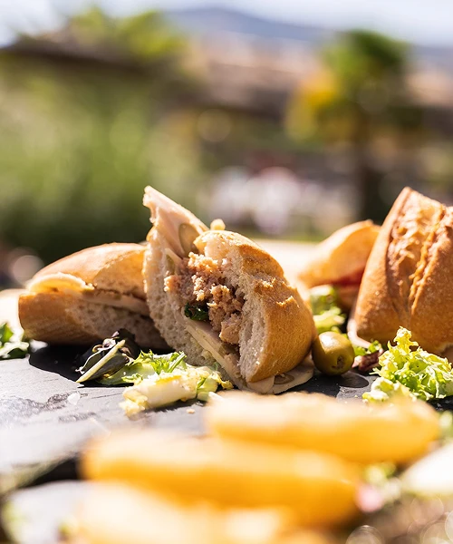 Bocadillo de at&uacute;n cortado con lechuga y aceitunas sobre una mesa al aire libre.