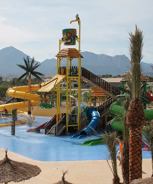 Parque acu&aacute;tico con toboganes y monta&ntilde;a al fondo en d&iacute;a soleado.