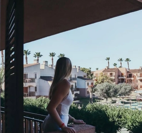 Mujer con vestido blanco contemplando un complejo de casas y palmeras al fondo.