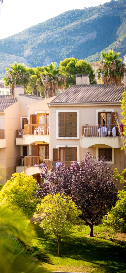 Edificios rodeados de &aacute;rboles con monta&ntilde;as al fondo en un d&iacute;a soleado.