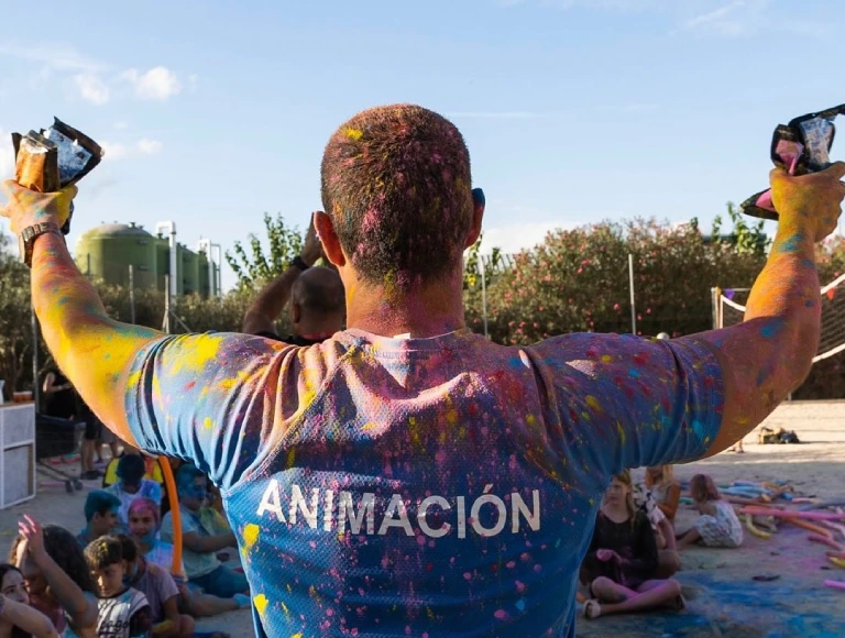 Persona con camiseta "ANIMACI&Oacute;N" cubierto de colores al aire libre.