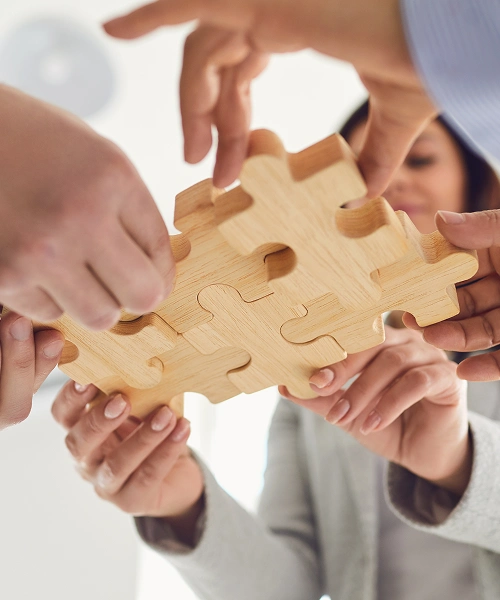 Manos uniendo piezas de madera de un rompecabezas en equipo.