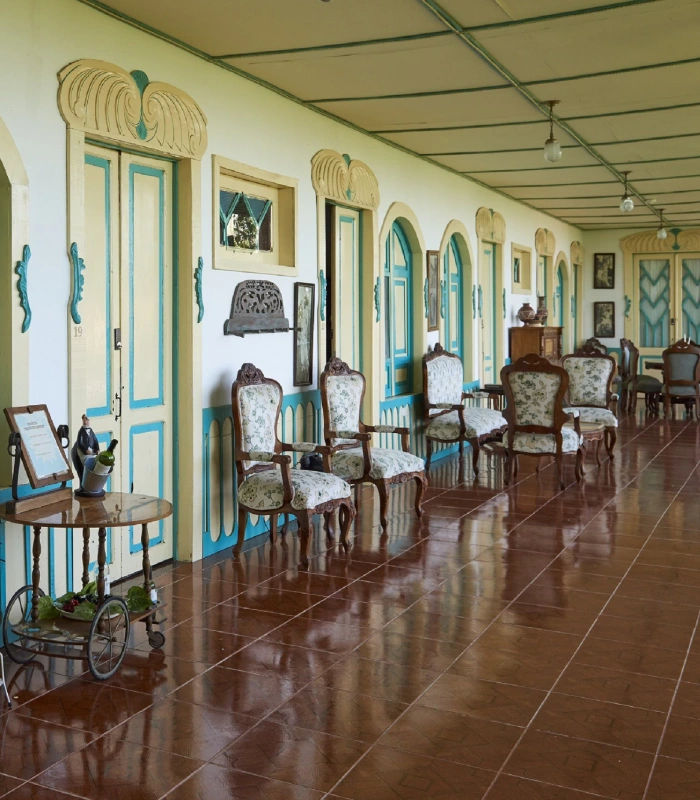 Pasillo con sillas antiguas y puertas azules en una casa colonial.