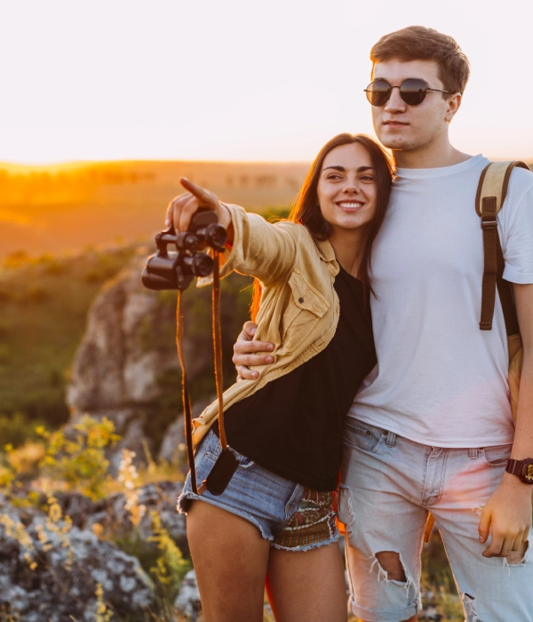 Pareja en la naturaleza al atardecer, mujer se&ntilde;ala con binoculares.
