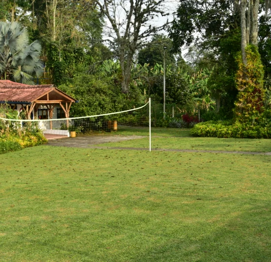 Campo de c&eacute;sped con red y caba&ntilde;a al fondo rodeada de &aacute;rboles.