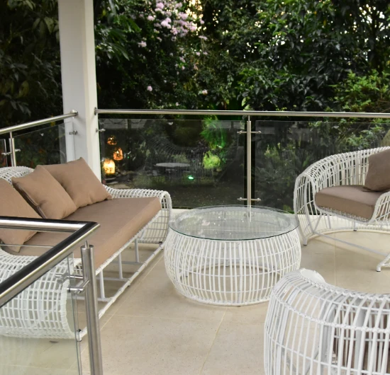 Terraza con muebles de mimbre blancos y cojines marrones, rodeada de plantas.