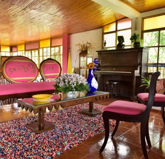 Sala vintage con piano, muebles rosas y alfombra colorida.