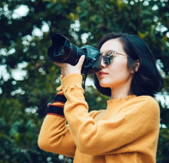 Persona con gafas de sol tomando fotos con una c&aacute;mara en un entorno verde.