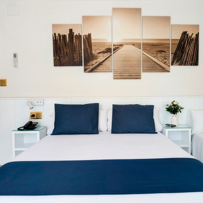 Dormitorio moderno con cama blanca, cojines azules y cuadros con paisaje des&eacute;rtico