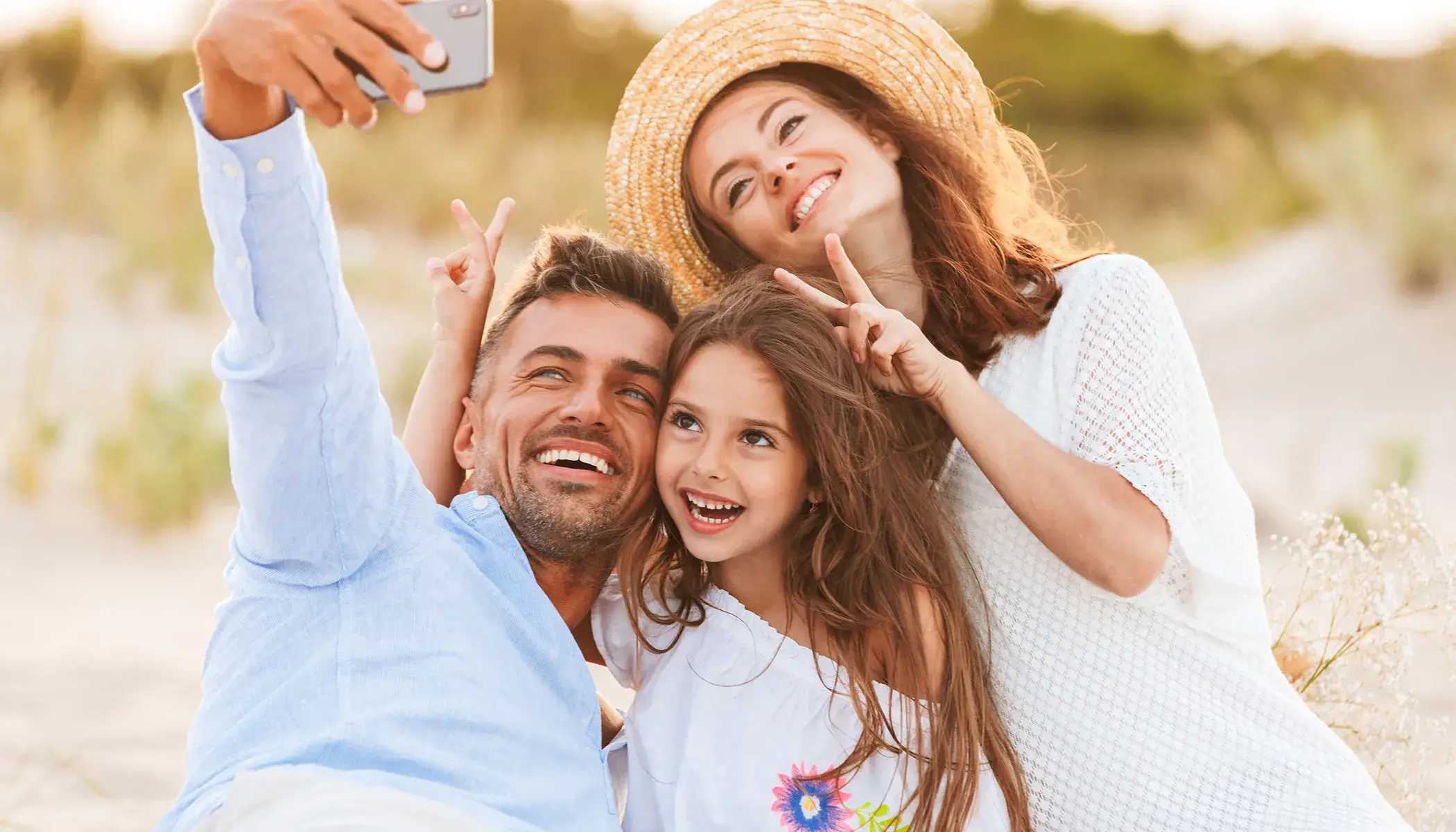 Familia sonriendo mientras se toma una selfie en la playa.
