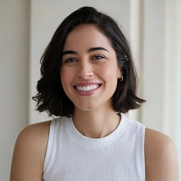 Una mujer de cabello oscuro sonr&iacute;e con un top blanco.