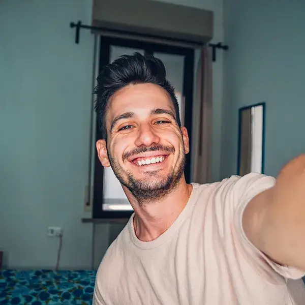 Hombre sonriendo mientras se toma una selfie en una habitaci&oacute;n.