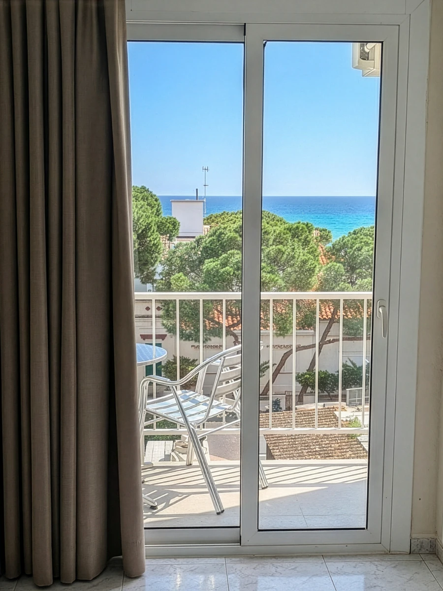 Vista desde una ventana a terraza con tumbonas y mar azul al fondo