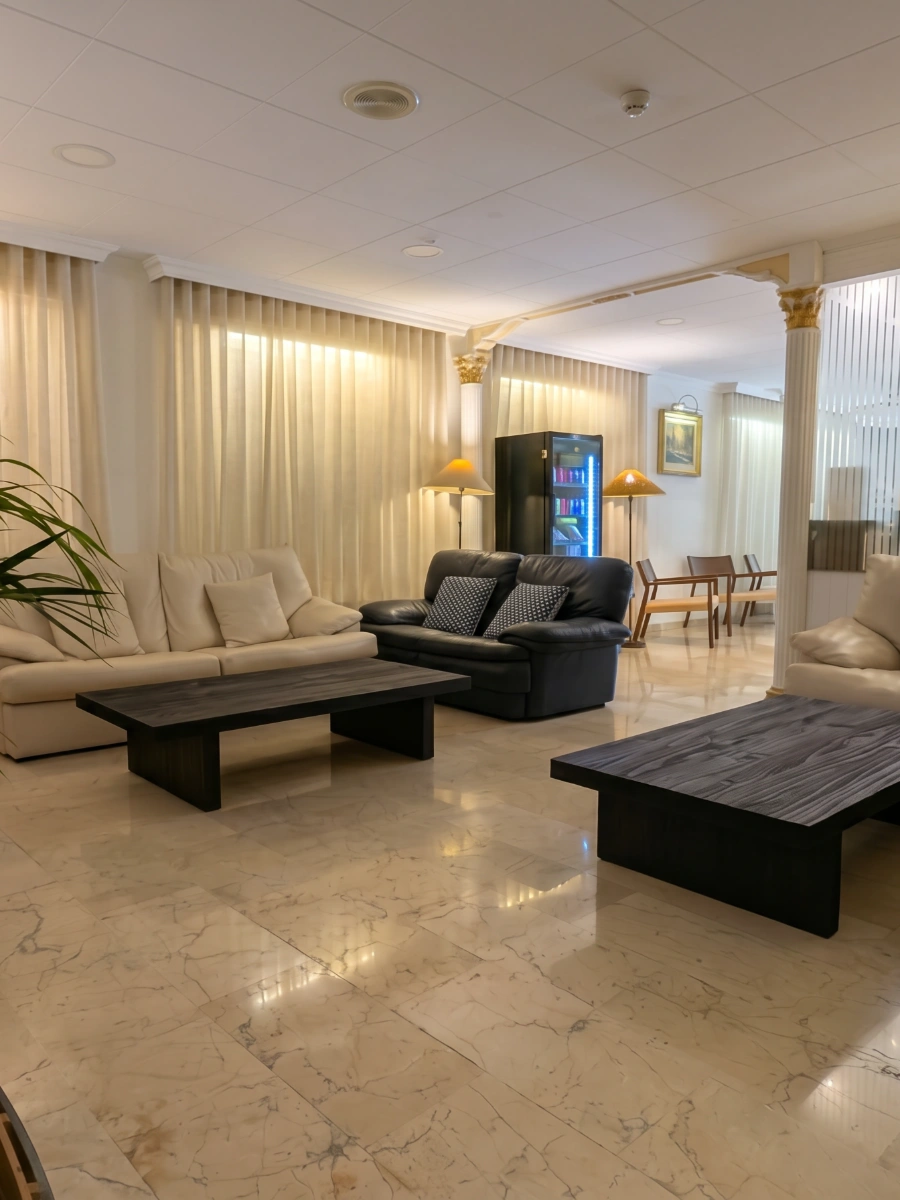 Sala de estar luminosa con sof&aacute;s, mesas de centro, TV y l&aacute;mparas.