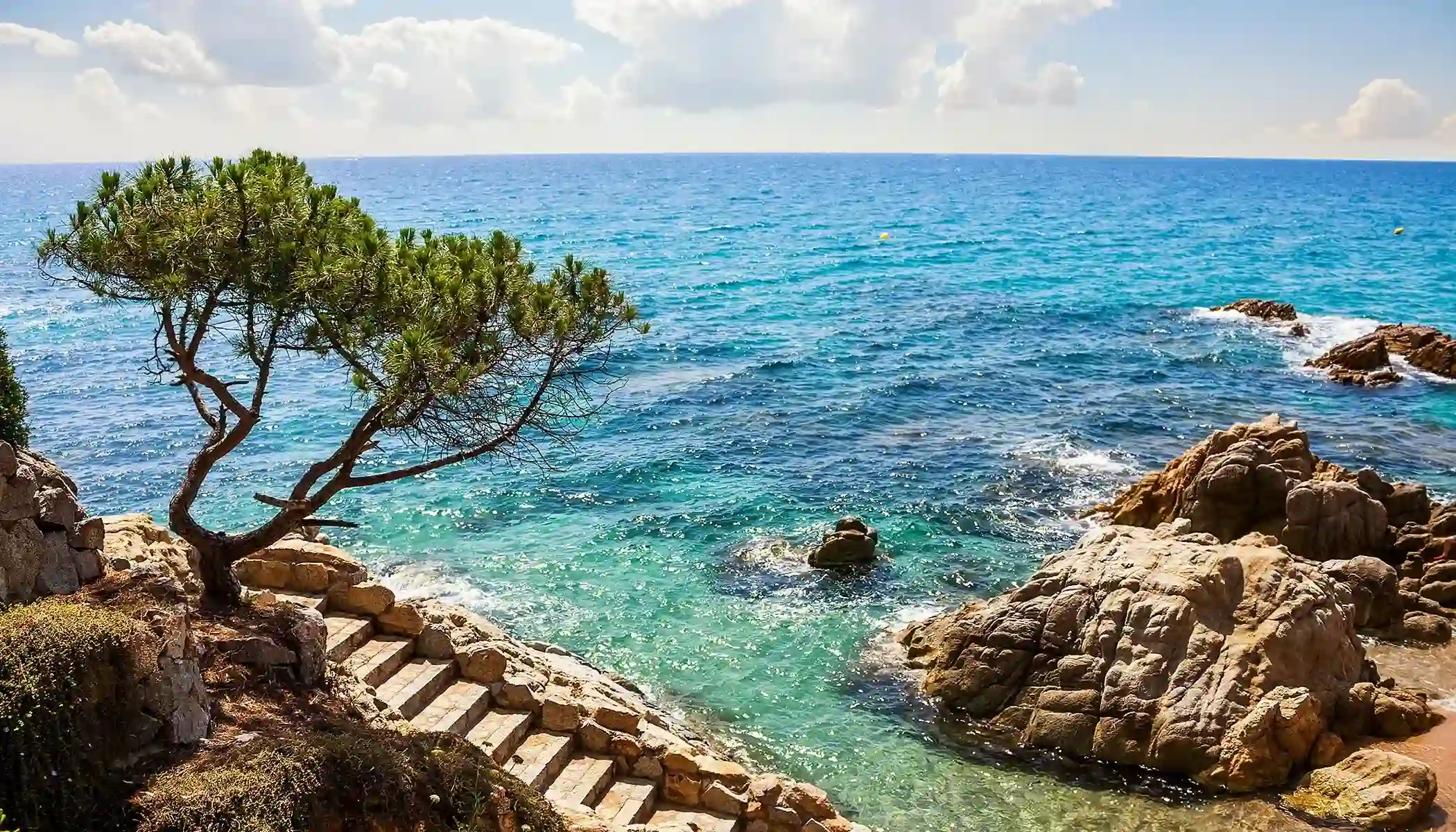 Escalera de piedra junto al mar con cielo azul y rocas costeras.