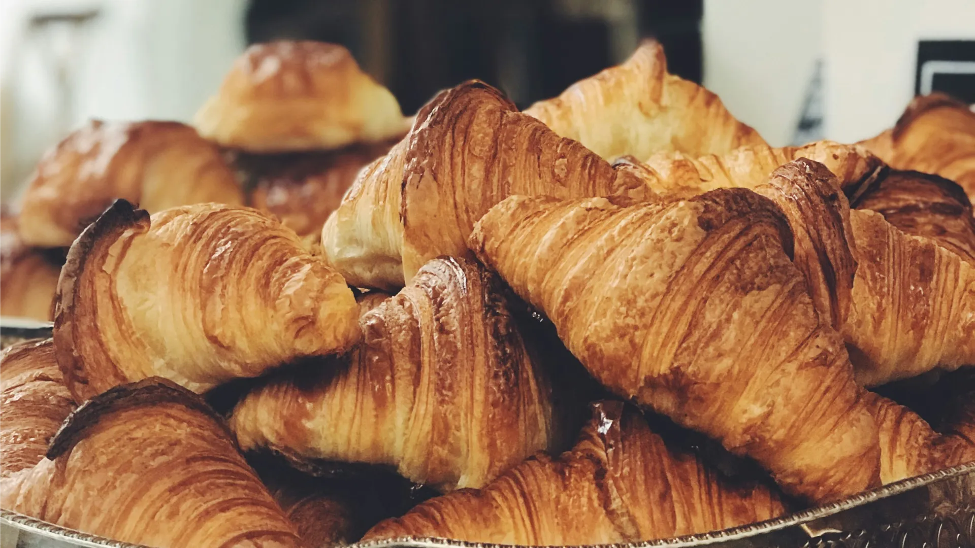 Muestra de croissants reci&eacute;n horneados en bandeja, fondo desenfocado.