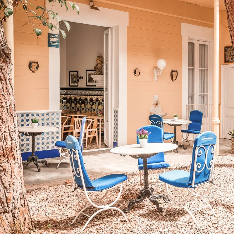 Patio con mesas y sillas azules rodeado de paredes color melocot&oacute;n y adornos.