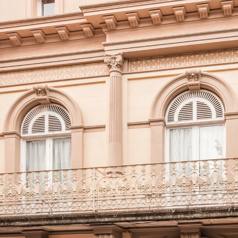 Fachada de edificio con columnas y ventanas de arco, en tonos beige.