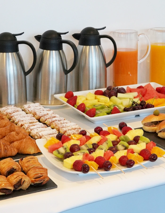 Buffet con caf&eacute;, jugos, frutas, cruasanes y pasteles en una mesa.
