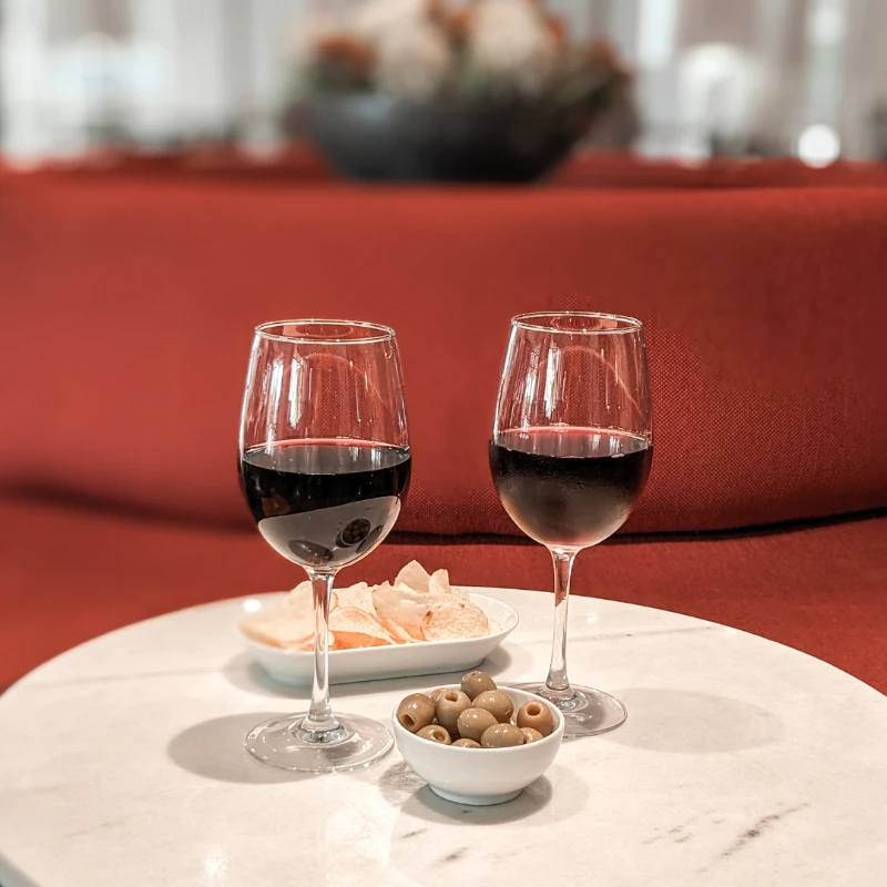 Dos copas de vino tinto, papas fritas y aceitunas sobre mesa de m&aacute;rmol blanca.