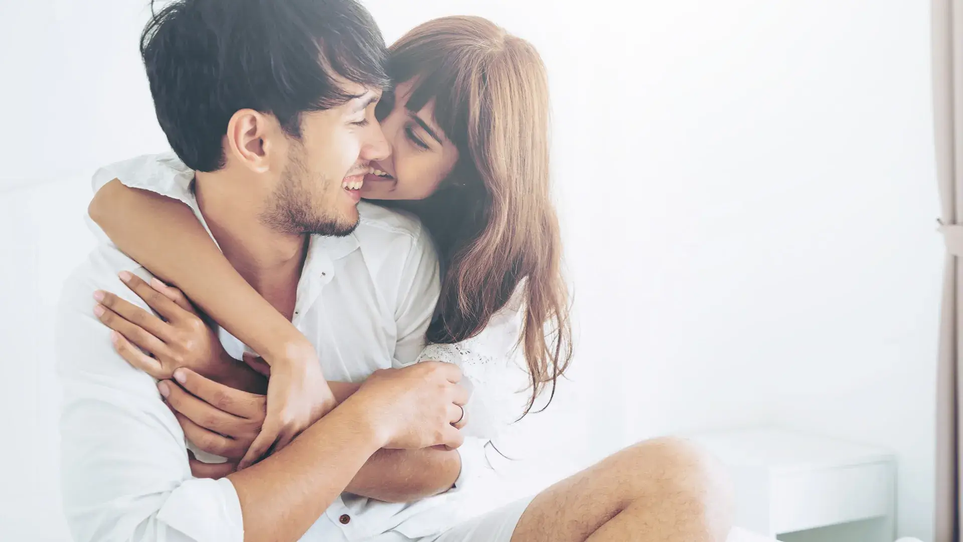 Pareja sonriendo y abraz&aacute;ndose en un ambiente blanco y luminoso.