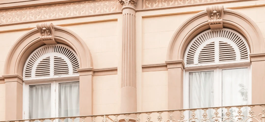 Ventanas con arcos y persianas en edificio de fachada beige ornamental.