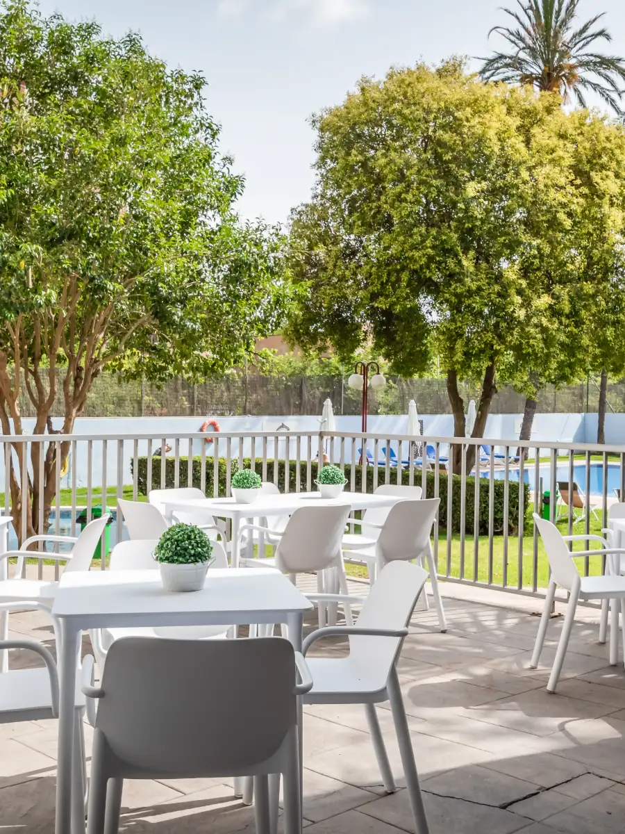 Muebles blancos en terraza junto a piscina y &aacute;rboles verdes.