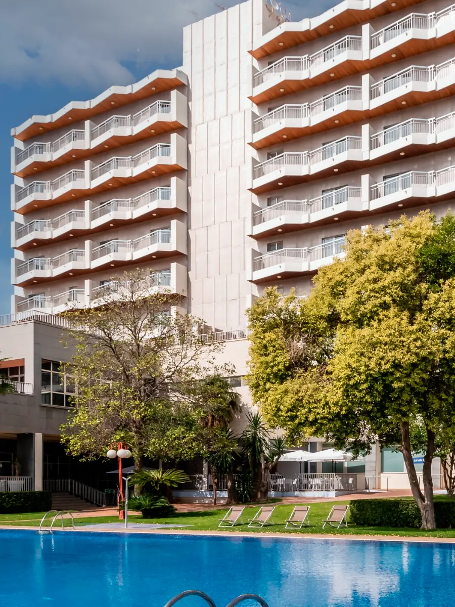 Edificio con balcones junto a piscina y &aacute;rboles en primer plano.