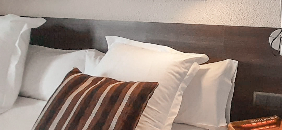 Cama con almohadas blancas y coj&iacute;n rayado marr&oacute;n.