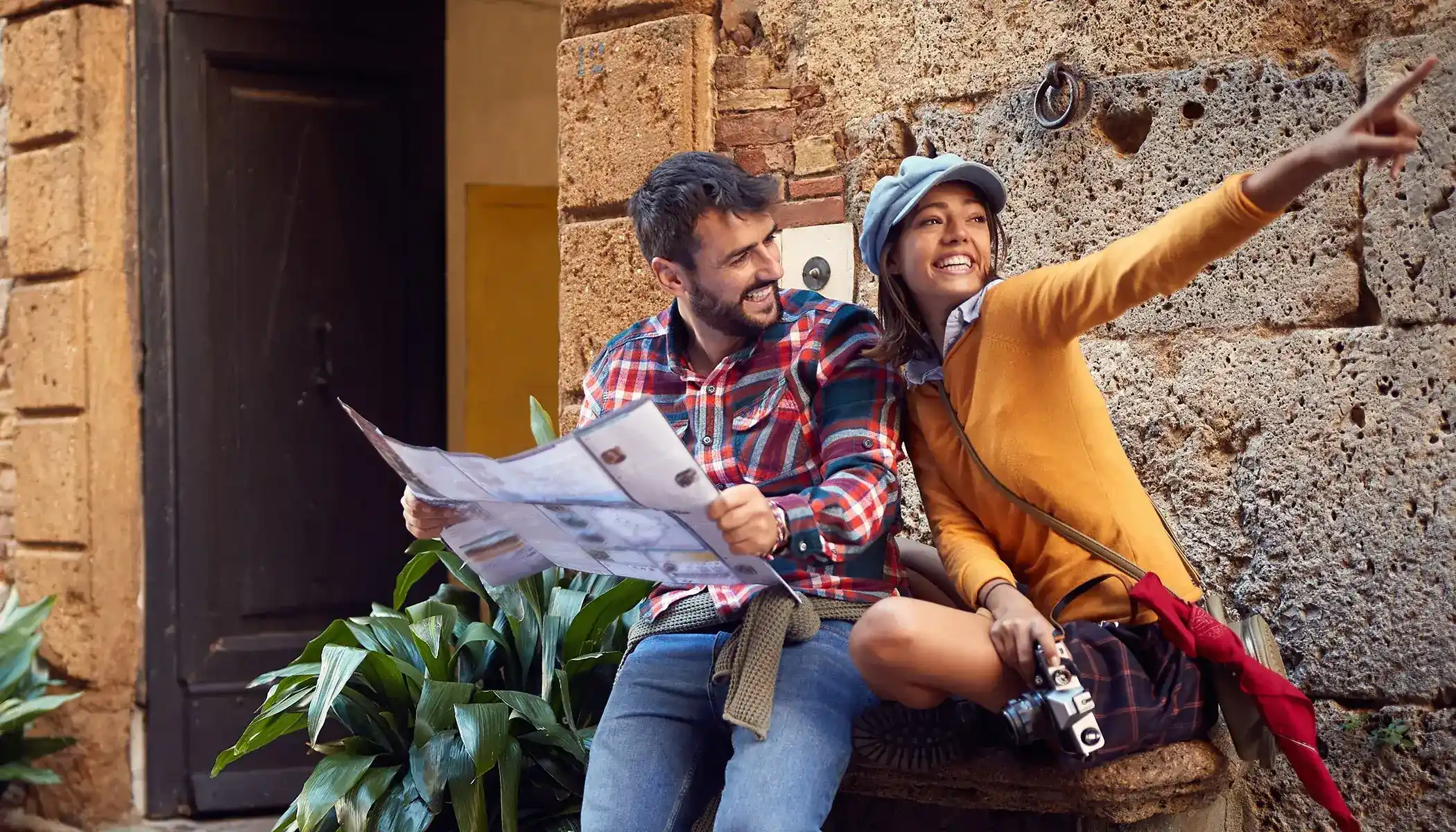 Pareja sonriendo con mapa y c&aacute;mara, explorando una ciudad hist&oacute;rica.
