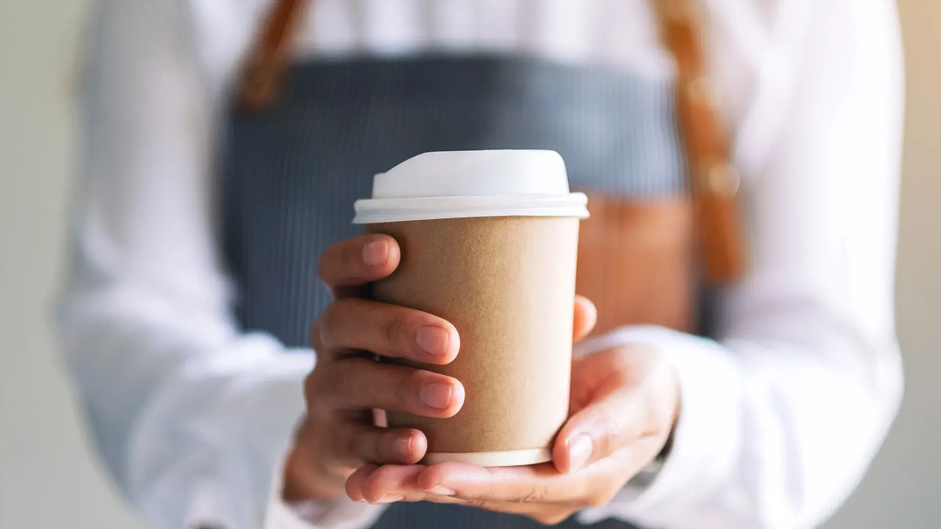 Persona sosteniendo un vaso de caf&eacute; desechable con tapa blanca.